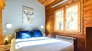 Une chambre à coucher avec un lit, des oreillers bleus, un plafond en bois, une fenêtre et un luminaire fixé au mur.