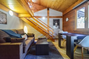 Relax in this spacious room with a high ceiling, featuring a comfortable sofa, dining area, and wooden staircase.