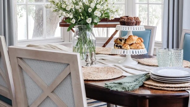 A dining area with a chandelier, white chairs, a vase with flowers, and a table set with plates, glasses, and pastries. - Spacious Luxurious Townhome - 2 Blocks to Forsyth! (Savannah)