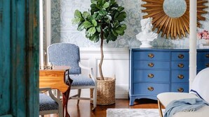 A room with a patterned wallpaper, a blue dresser, a round mirror, a plant, a polka-dotted chair, and a wooden floor. - Spacious Luxurious Townhome - 2 Blocks to Forsyth! (Savannah)