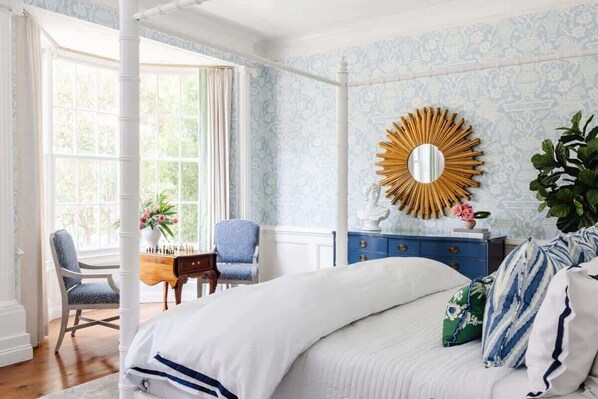 Un dormitorio con una cama grande, una tocador con espejo, una silla y una ventana con cortinas.