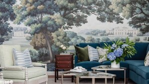 A living room with a large mural of a landscape, a blue sofa, a green armchair, a wooden side table, and a coffee table. - Spacious Luxurious Townhome - 2 Blocks to Forsyth! (Savannah)