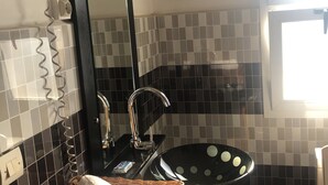 Une salle de bain avec un lavabo noir, un miroir, un sèche-cheveux et un panier en osier contenant une serviette.