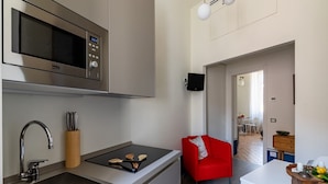 A modern kitchen with a microwave, sink, and red chair. There is a dining area with a white table and a television mounted on the wall.