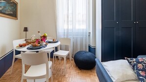 A small, cozy room with a dining table set for two, a bed with a floral pillow, and a large wardrobe.