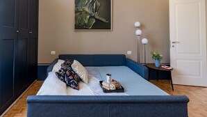 A bedroom with a large bed, a dark wardrobe, a painting on the wall, and a bedside table with a lamp.