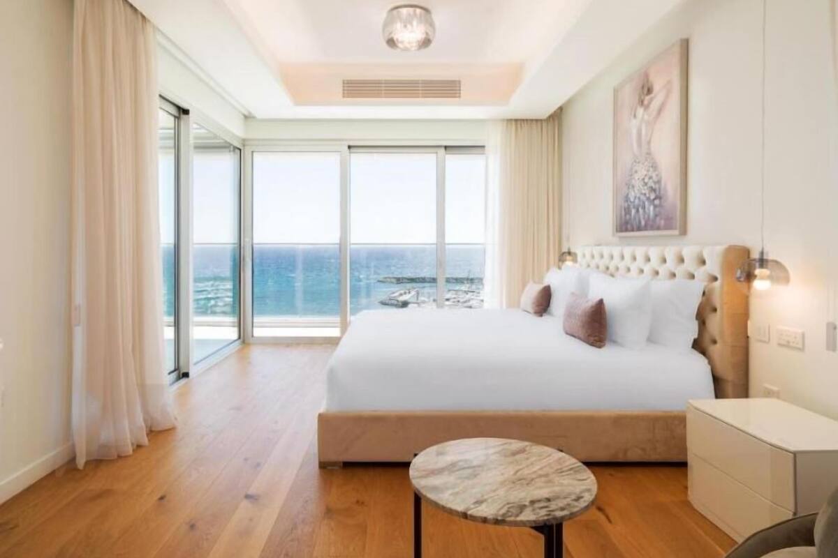 Un dormitorio con una cama grande, una mesa redonda y vista al océano.