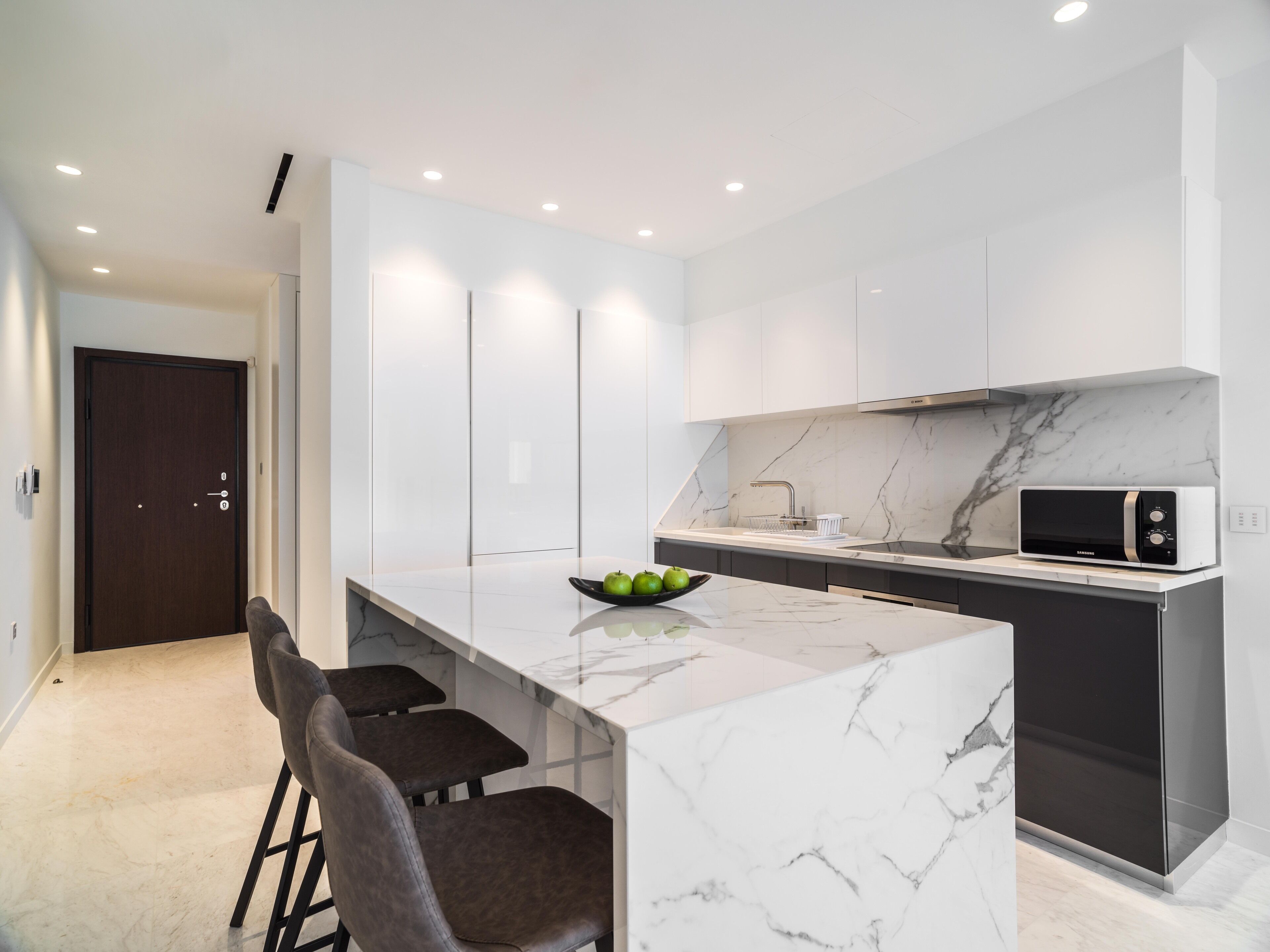 A modern kitchen with a marble countertop, a built-in microwave, and a bowl of green apples.