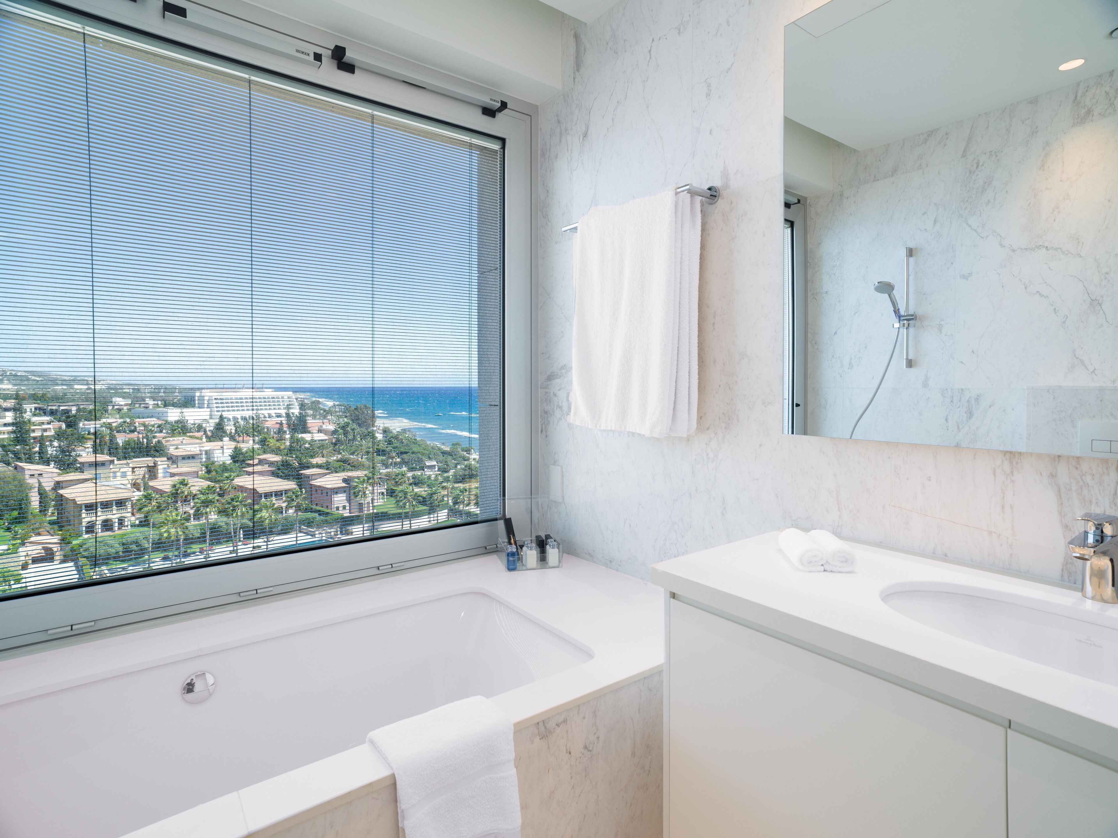 Un baño moderno con una bañera grande, un lavamanos doble y un ventanal con vistas a un pueblo costero.