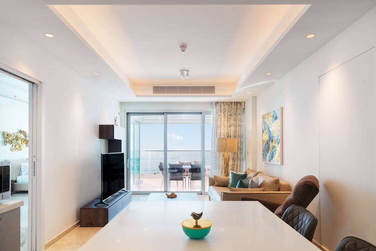 Una sala de estar moderna con una mesa blanca grande, un televisor de pantalla plana y un sofá.