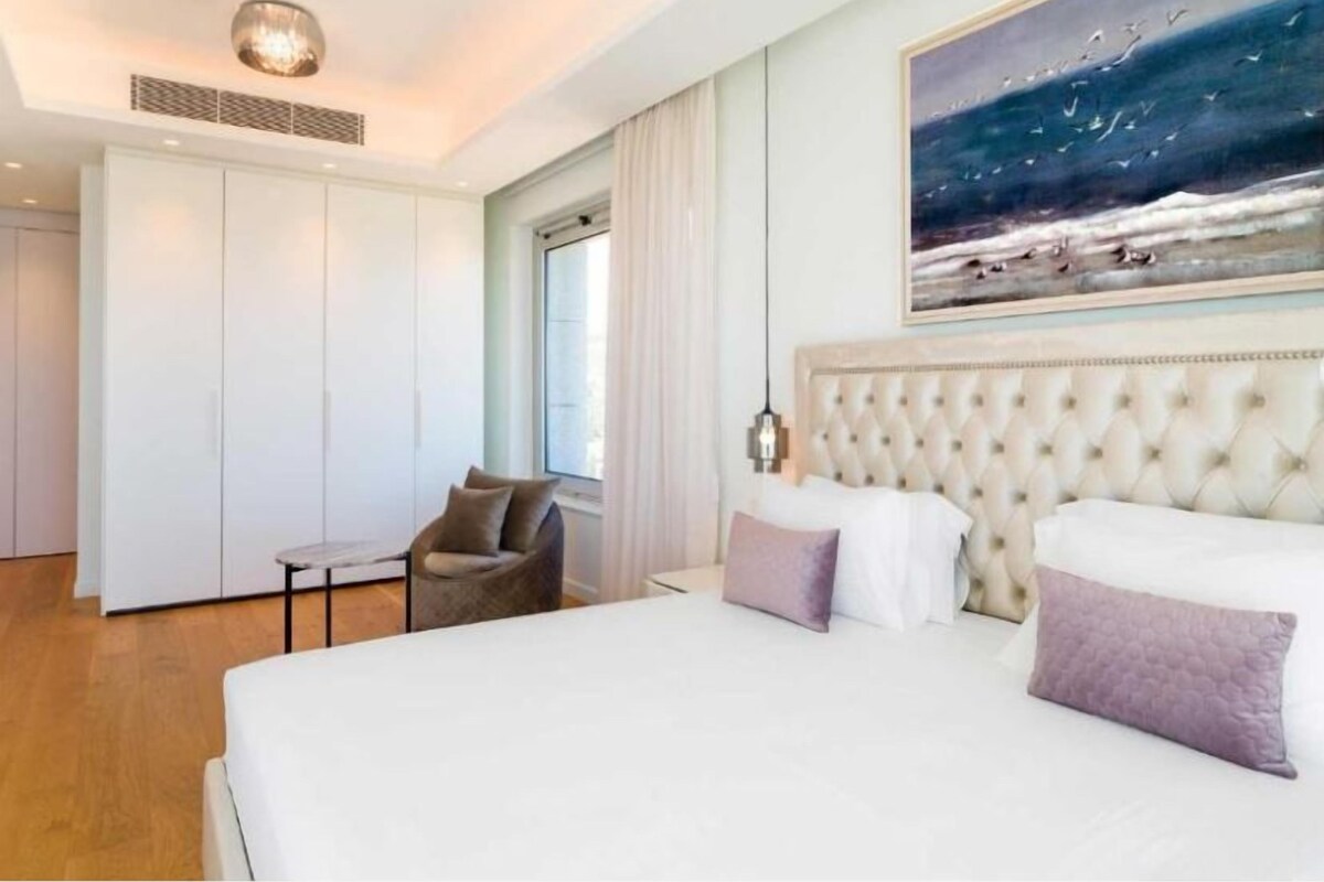 Une chambre à coucher avec un grand lit, une chaise, une armoire et un tableau représentant des oiseaux accroché au mur.