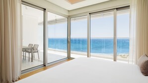 Een slaapkamer met een groot bed, een balkon met uitzicht op zee, en een eethoek met stoelen.