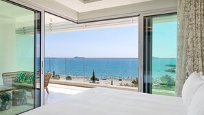 Een moderne hotelkamer met een groot bed en een glazen deur naar een balkon met uitzicht op zee.