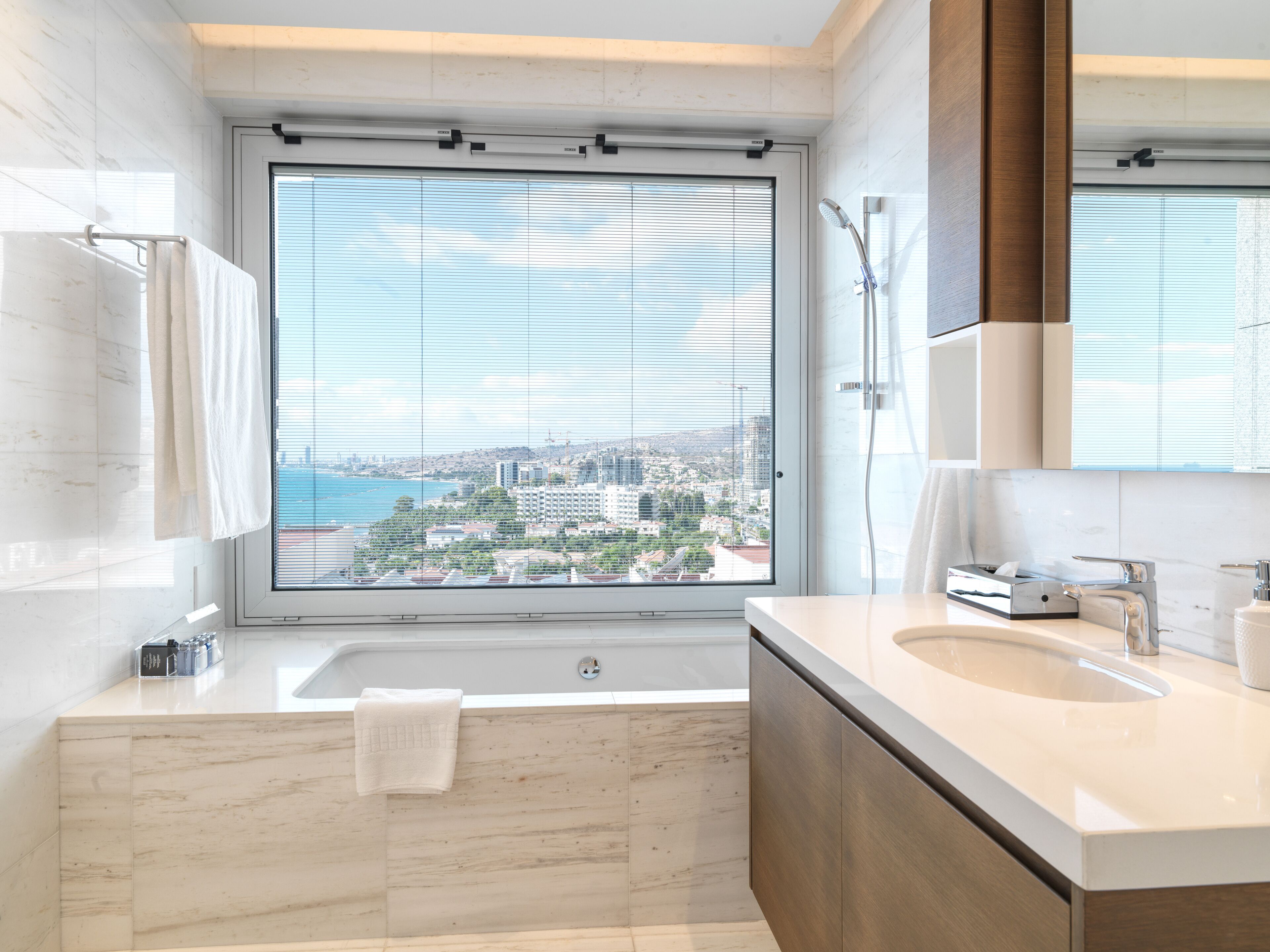 A modern bathroom with a large window, a bathtub, and a vanity with a sink.