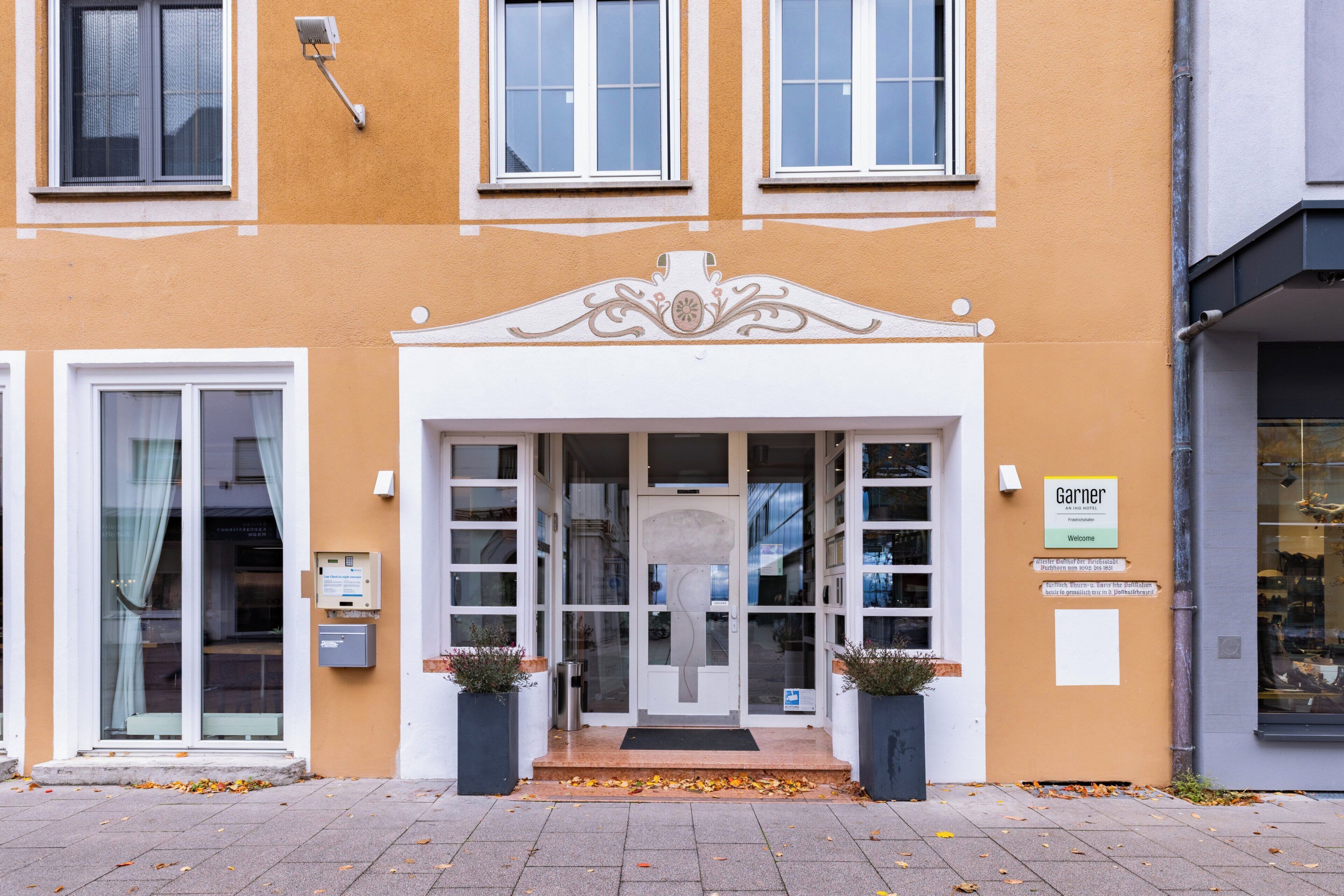Ein Gebäude mit gelber Fassade, einem zentralen Eingang mit Glastüren und einem Schild mit der Aufschrift 'Garner'.