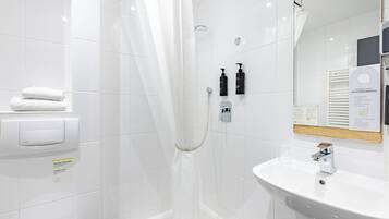 A modern bathroom with a white bathtub, a sink, a shower with a glass door, and a mirror with a wooden frame.