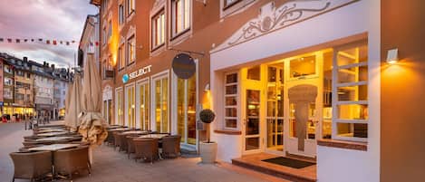A hotel with outdoor seating, a signboard, and a well-lit entrance.