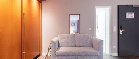 A room with a grey sofa, wooden wardrobe, and a door with a lock.