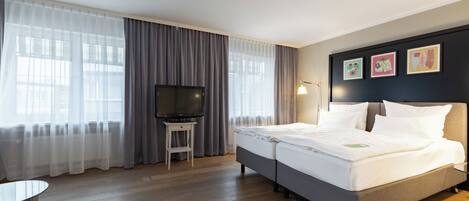 A hotel room with a bed, a TV, a small table, and curtains.
