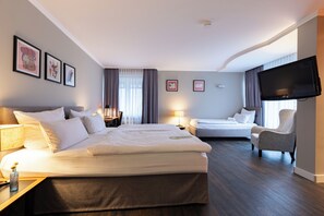 Habitación de hotel con una cama grande, una cama más pequeña, una silla, un televisor y cuadros en la pared.