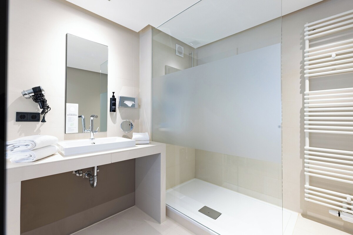 Un baño moderno con cabina de ducha de vidrio, tocador con espejo y perchero.