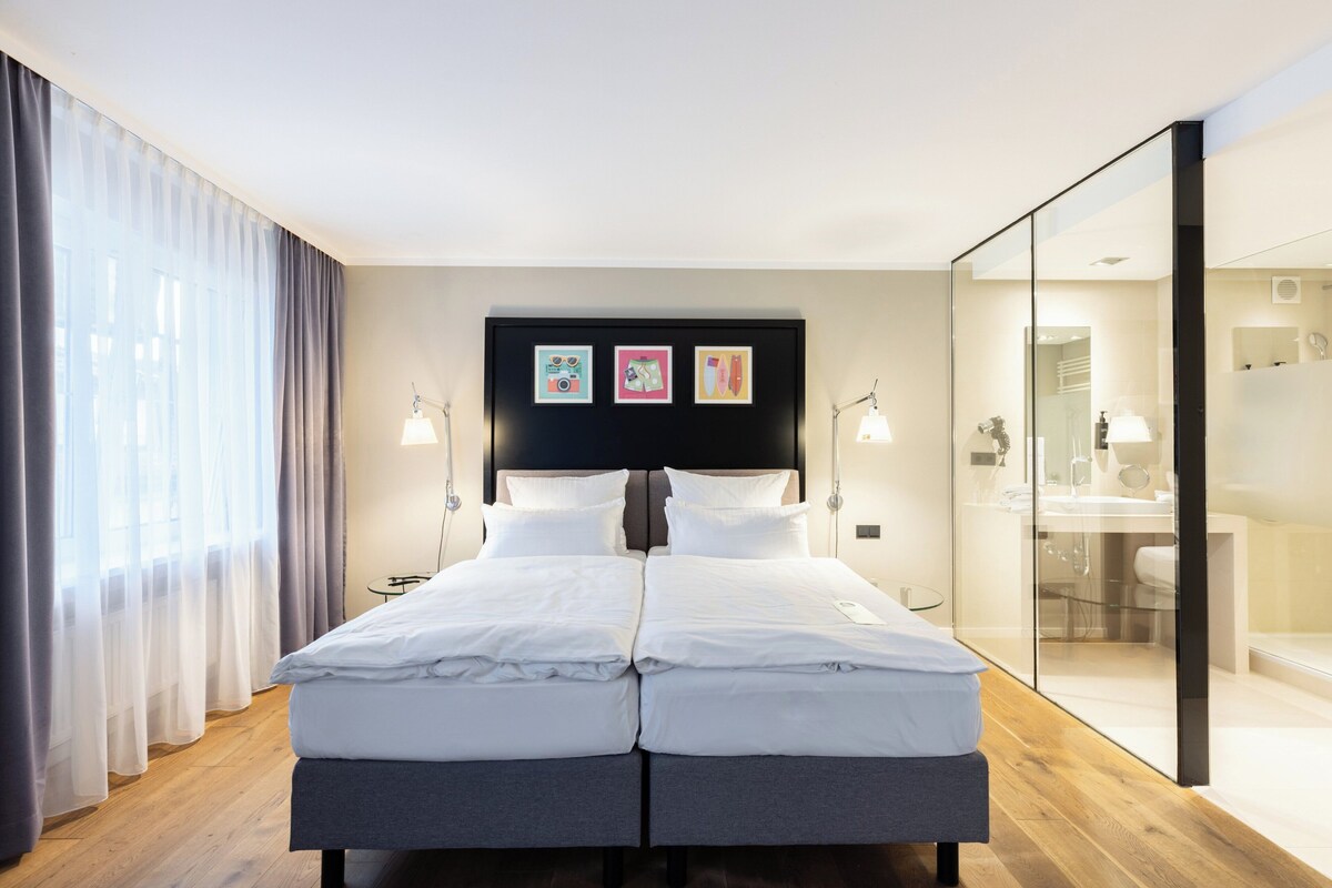Una cama doble con cabecera oscura, lámparas de noche y una obra de arte en la pared.