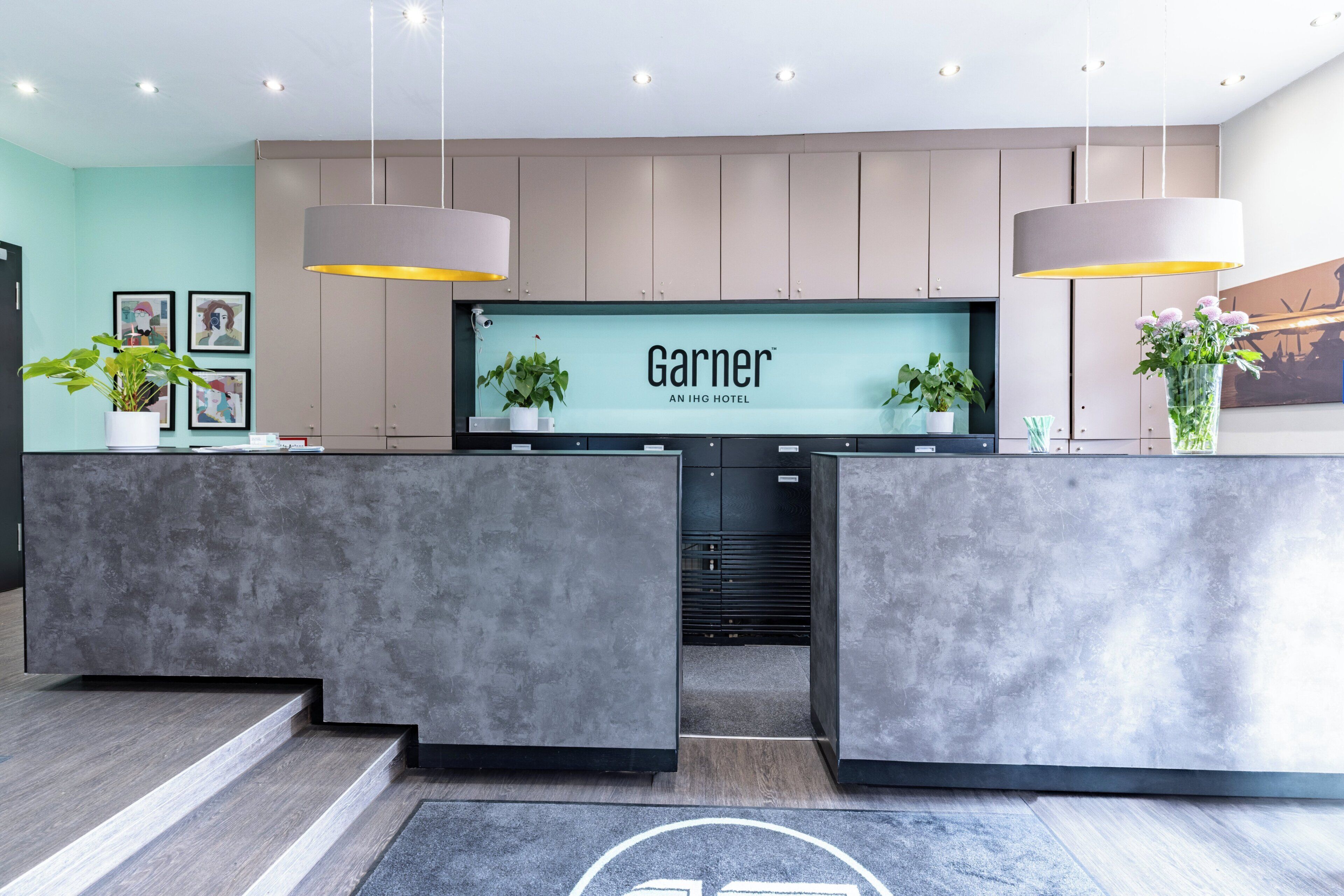 A hotel reception desk with a modern design, a large screen displaying the hotel name, and two pendant lights.