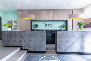Un mostrador de recepción de hotel con diseño moderno, una pantalla grande que muestra el nombre del hotel y dos lámparas colgantes.