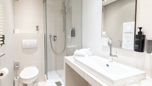 A modern bathroom with a glass-enclosed shower, a white sink, and a large mirror. - Garner Hotel Friedrichshafen by IHG (Friedrichshafen)