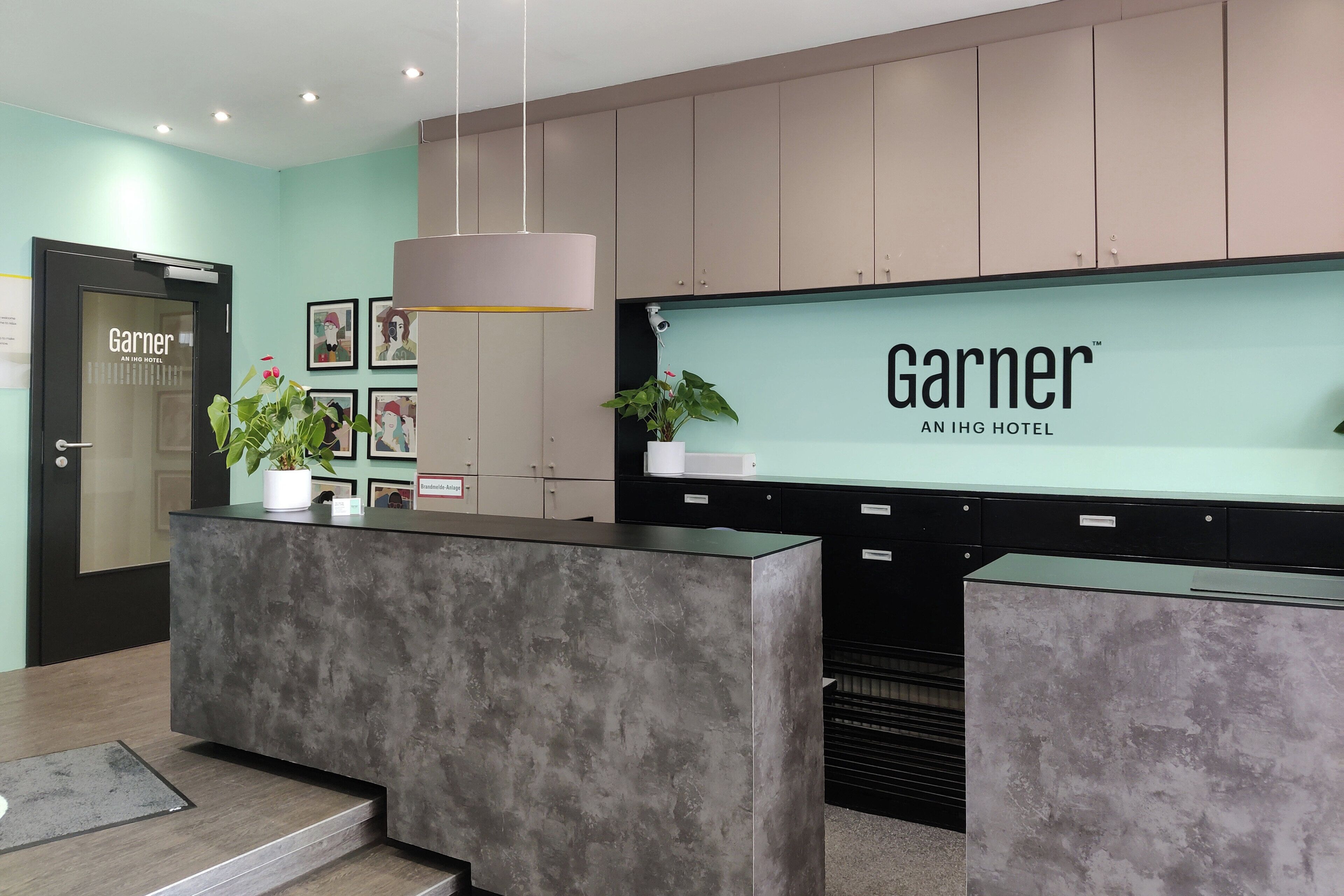 A hotel reception desk with a modern design, a sign reading 'Garnier AN IHG HOTEL,' and a potted plant on the counter.