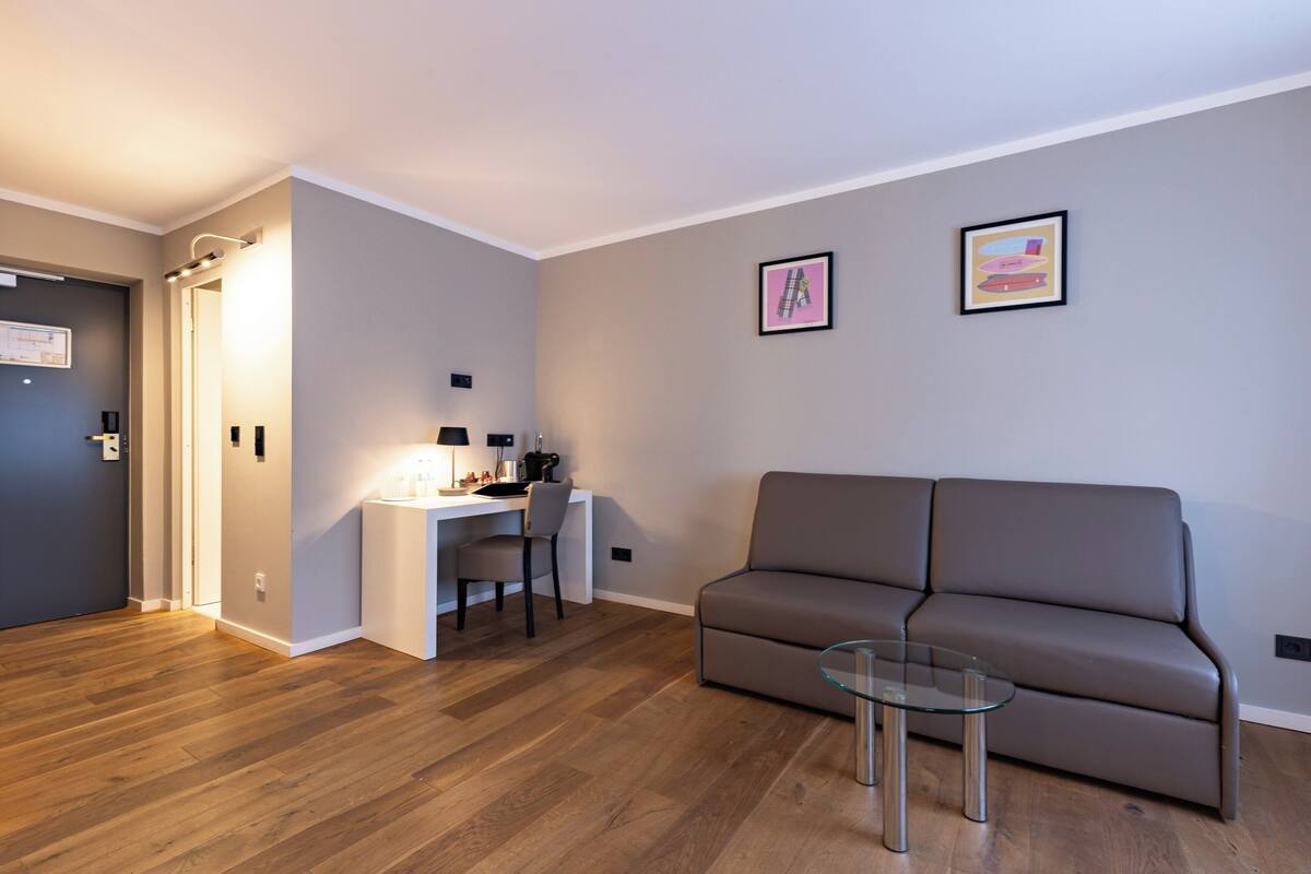 A modern living room with a sofa, a glass coffee table, and a desk with a chair.