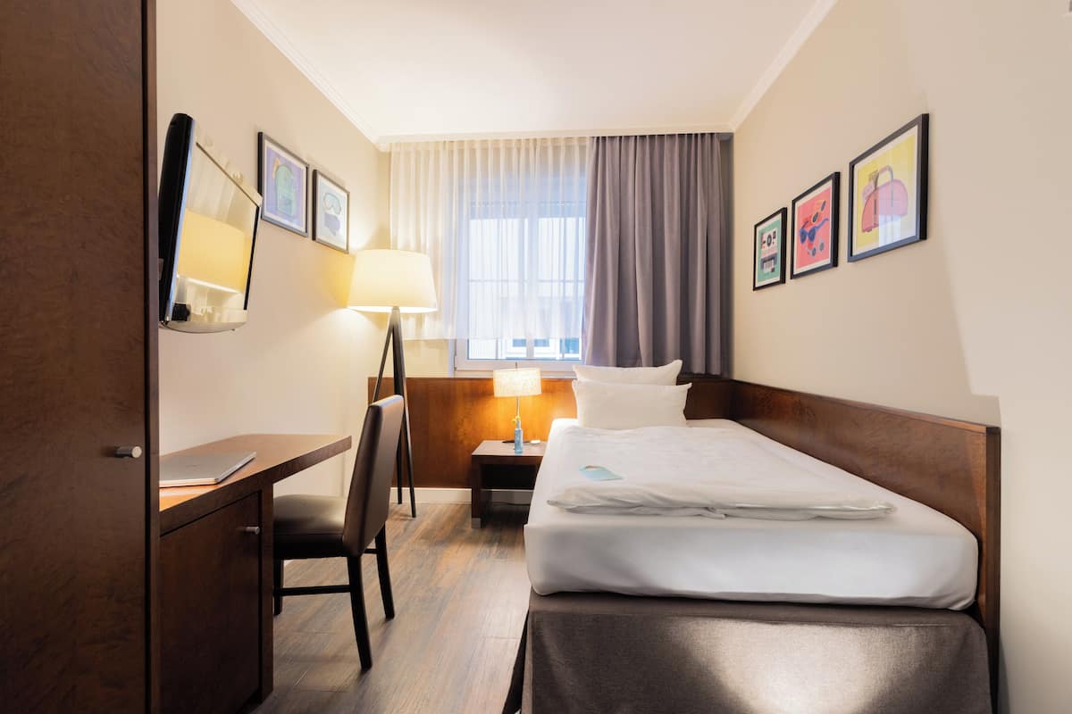 A hotel room with a bed, desk, chair, lamp, and artwork on the walls.