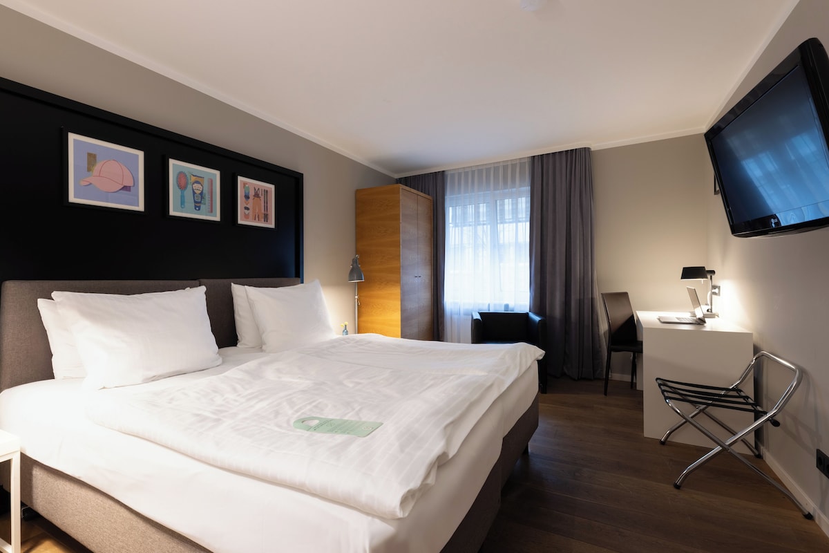 Habitación de hotel con una cama grande, un escritorio, una silla, un televisor y obras de arte en la pared.