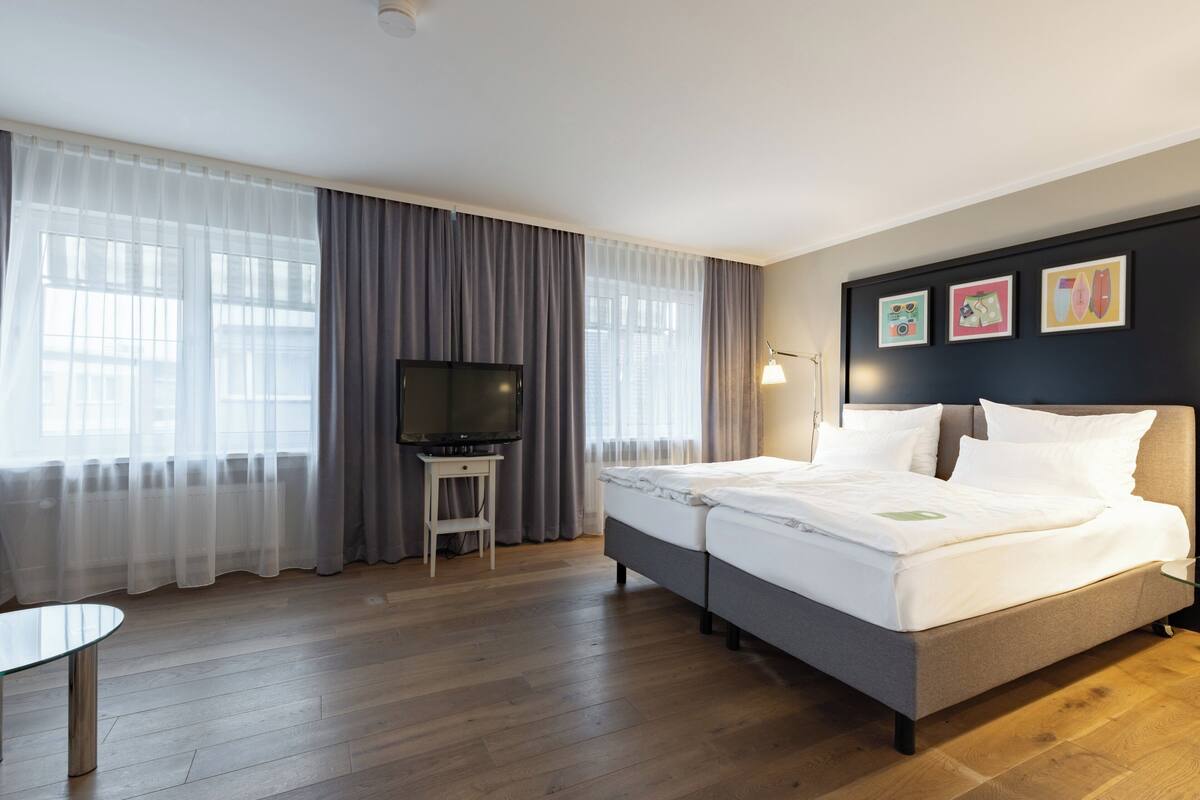 A hotel room with a bed, a TV, a small table, and curtains.
