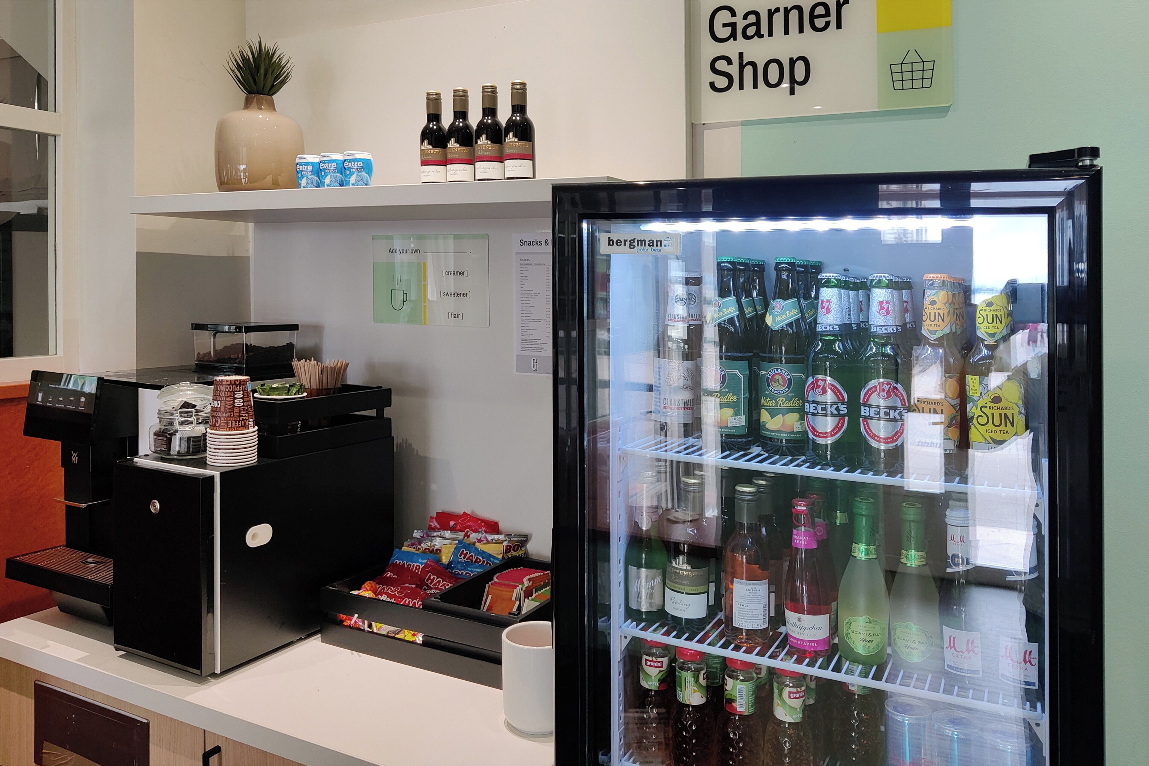 Un refrigerador con bebidas variadas, una máquina de café y un cartel que indica 'Garner Shop'.