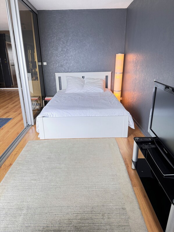 Un dormitorio moderno con una cama grande, un televisor sobre un mueble bajo y un cerrojo corredizo que da a un baño.