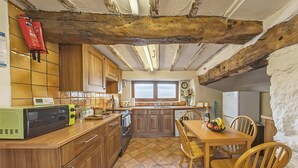 Una cocina con armarios de madera, piso de baldosas, una mesa de comedor de madera con sillas, un microondas y un refrigerador.