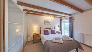 Un dormitorio con cama, lámparas de noche, cabecera de madera, radiador y ventana con cortinas.