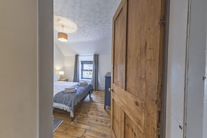 A bedroom with a wooden floor, a bed with a blue blanket, a hanging light fixture, and a window with curtains.