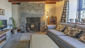 Ein gemütliches Wohnzimmer mit Kamin aus Stein, einer Couch mit gemusterten Kissen, einem Bücherregal und einem Fernseher.