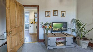 Ein Zimmer mit Holztür, Fernseher auf einem Schrank, einer Topfpflanze und gerahmten Bildern an der Wand.