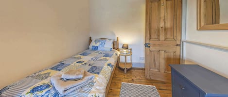 A small, cozy bedroom with a single bed, a bedside table with a lamp, a wooden wardrobe, and a door.