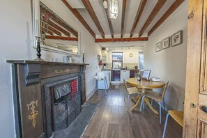 A kitchen with a fireplace, wooden beams, and a dining area with chairs and a table.