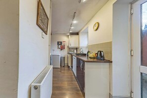 Un pasillo estrecho que conduce a una cocina con un radiador, un reloj y un refrigerador pequeño.