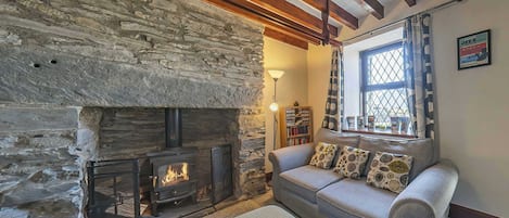 A cozy living room with a stone fireplace, a sofa with patterned cushions, and a window with patterned curtains.