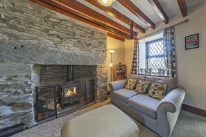 A cozy living room with a stone fireplace, a sofa with patterned cushions, and a window with patterned curtains.