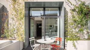 Un área de estar moderna al aire libre con una mesa y dos sillas, una entrada con puerta de vidrio y vistas al interior.