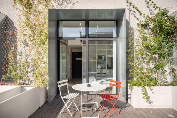 Uma área de estar moderna ao ar livre, com mesa e duas cadeiras, porta de vidro e vista para o interior.