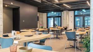 Una sala de conferencias moderna con varias mesas y sillas, ventanas amplias y una señal de salida visible.