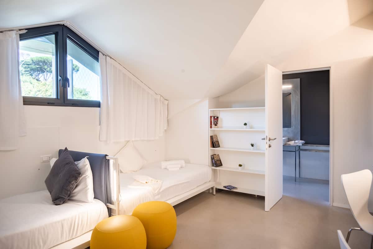 A modern bedroom with a bed, a small desk, and a view of the kitchen.